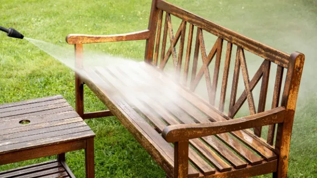 man cleaning garden bench with high-pressure cleaner