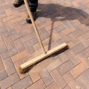 man sweeps sand in joints of terrace