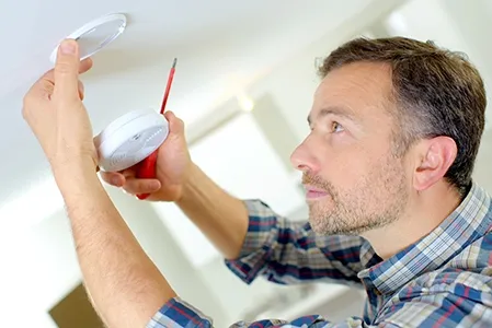 man fixes smoke detector to ceiling